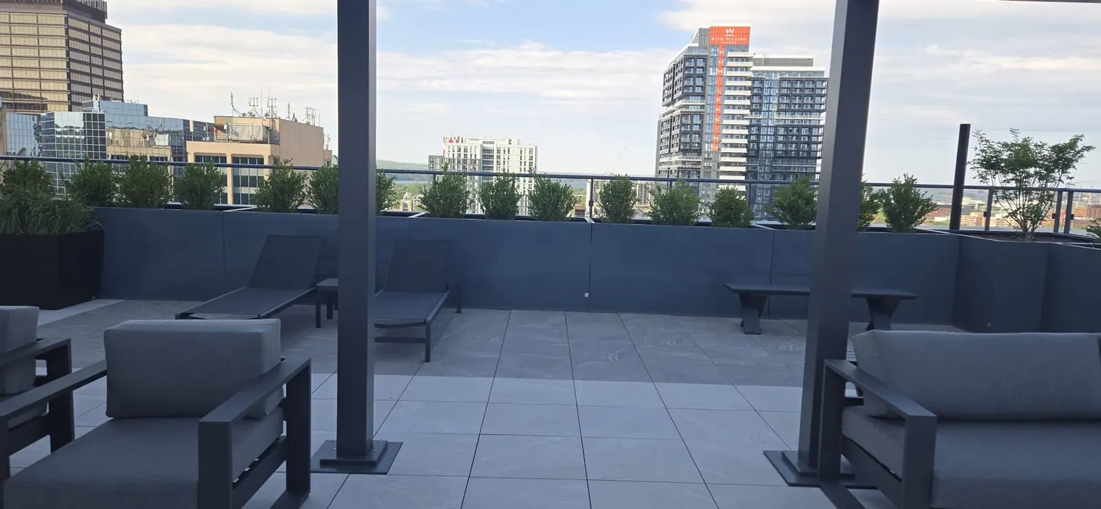 View from under the rooftop pergola toward downtown high-rises, lounge chairs framing either side.
